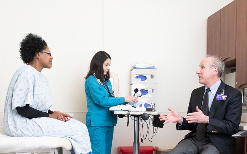 A person sits while talking to two health care professionals at a doctor's office.